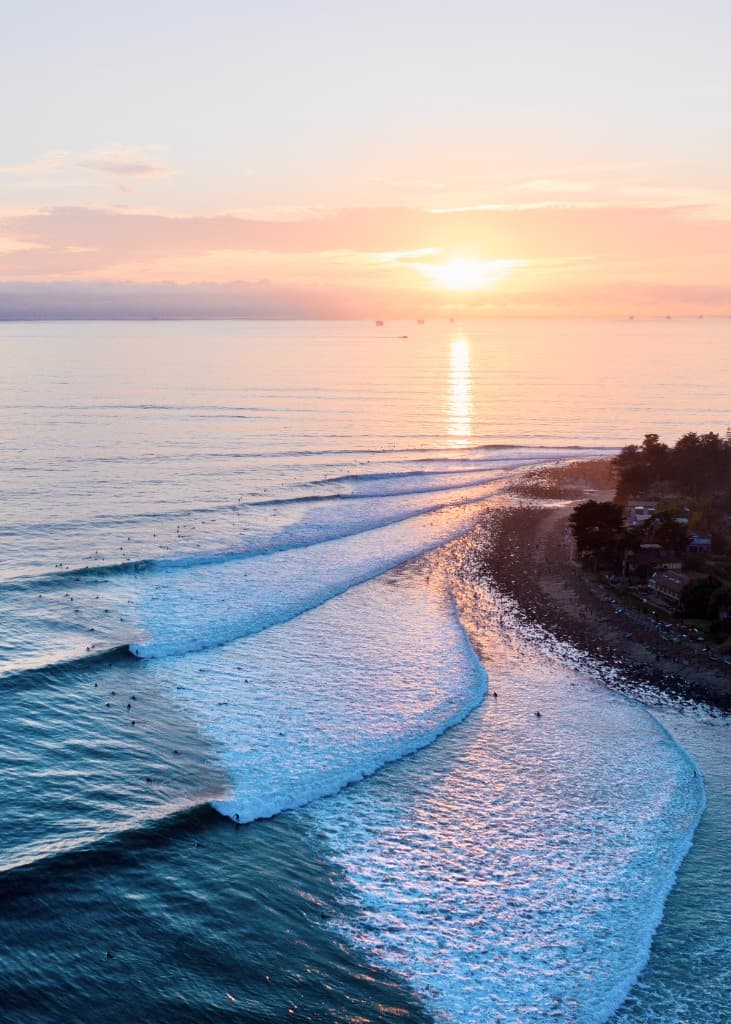 Aerial view of a coastline at sunset with surfers in the lineup