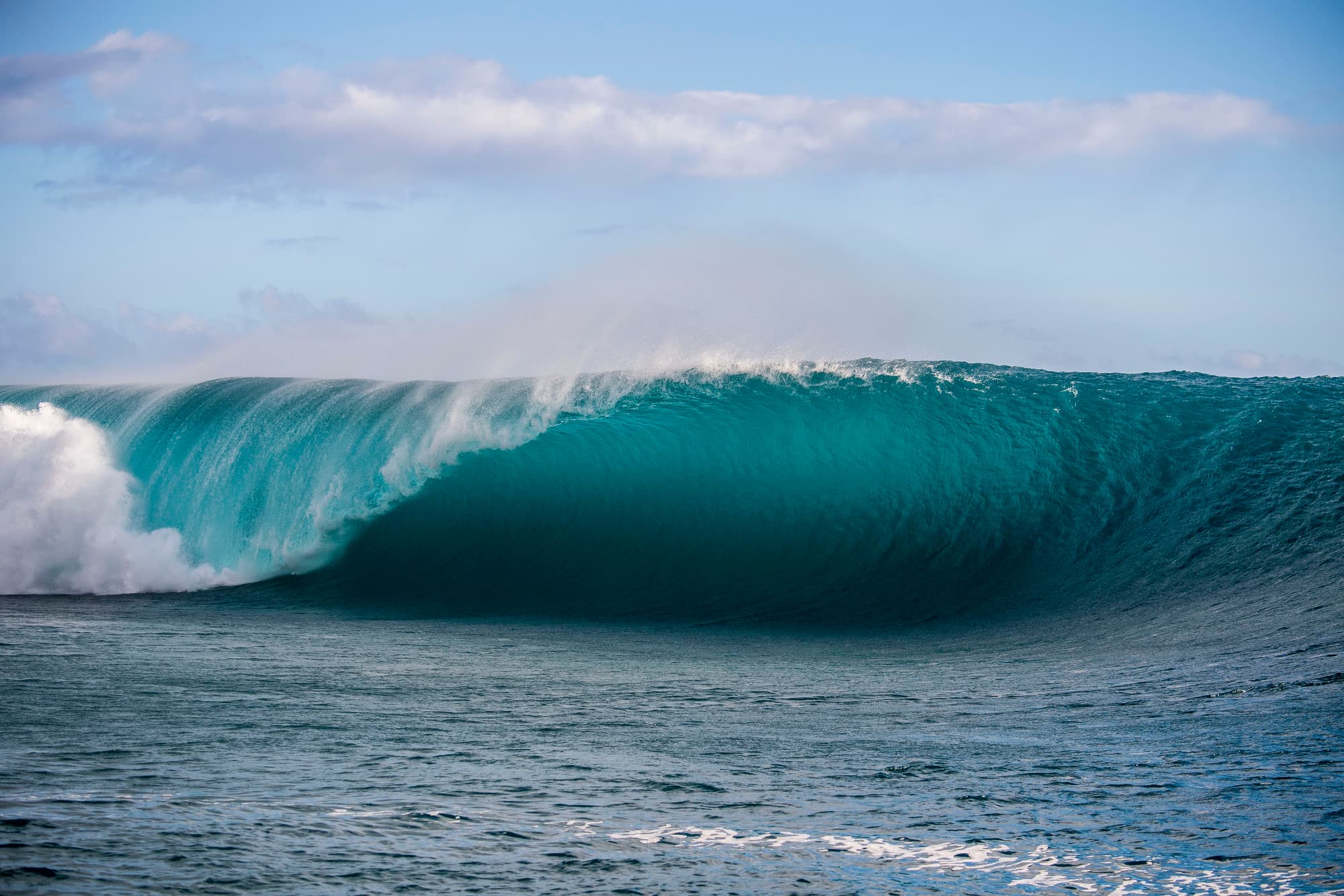 A large turquoise wave under a pale sky