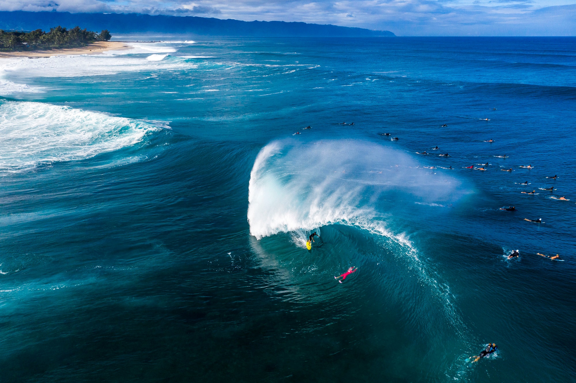 Aerial view of a barreling wave with surfers in the lineup