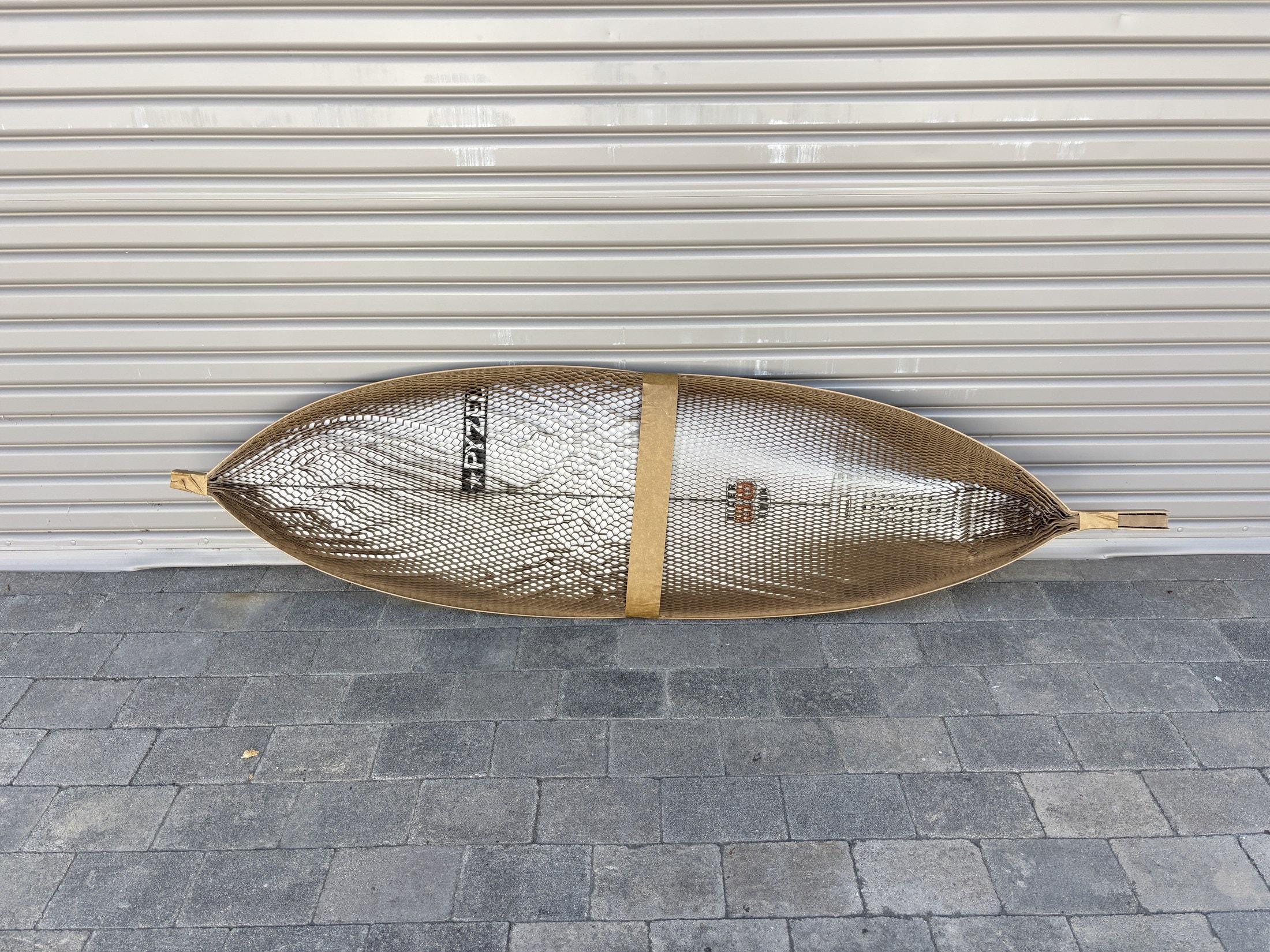 A Pyzel surfboard wrapped in honeycomb packing paper against a shop door